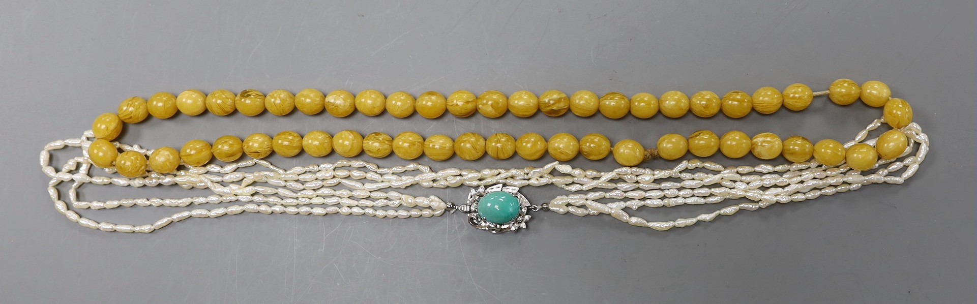 A multi-strand 'rice pearl' necklace with 18k white metal and turquoise set clasp, 66cm and an amber necklace.